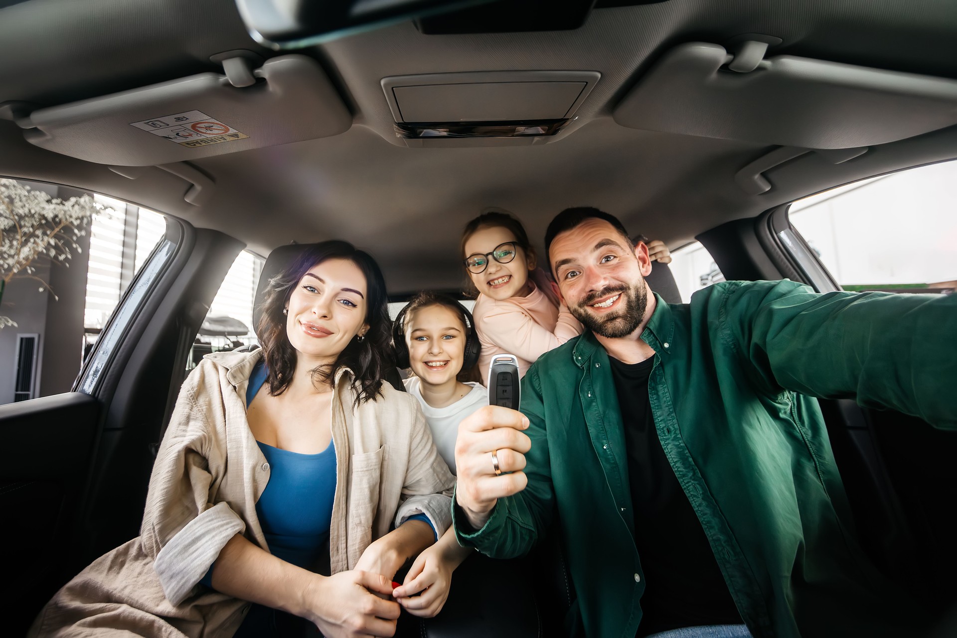 Happy married couple with two daughters are happy after buying a new car in a modern car dealership.